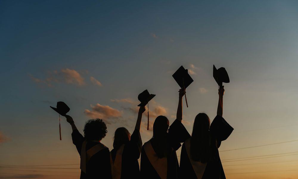 College graduates lifting their graduation caps.