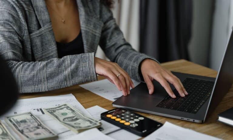 Employee typing at a laptop with a calculator.