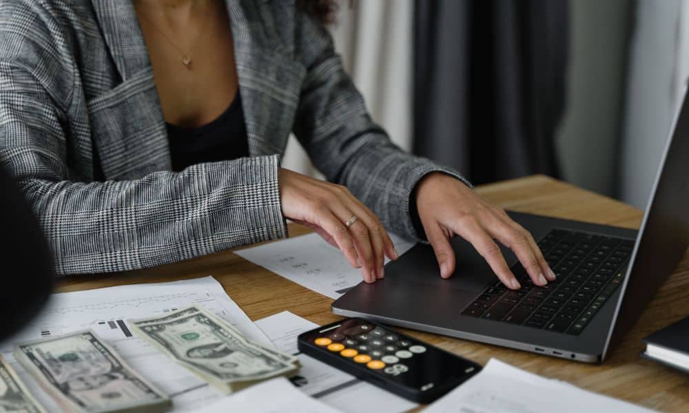 Employee typing at a laptop with a calculator.