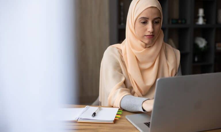 Employee typing at laptop with a notebook and pen.