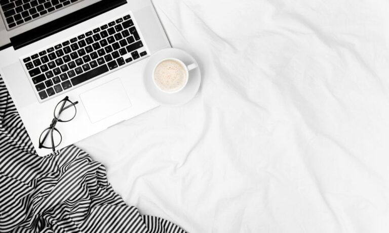 Photo of a laptop on a bed with a cup of coffee.