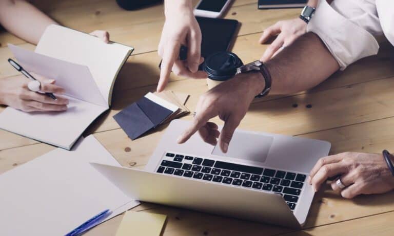 Photo of a team working together and pointing at a laptop screen.