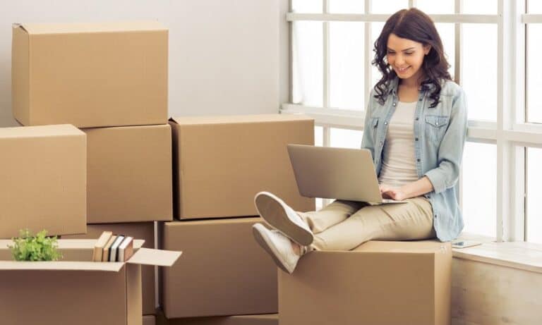 Woman sitting on moving boxes on computer