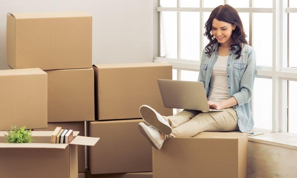 Woman sitting on moving boxes on computer