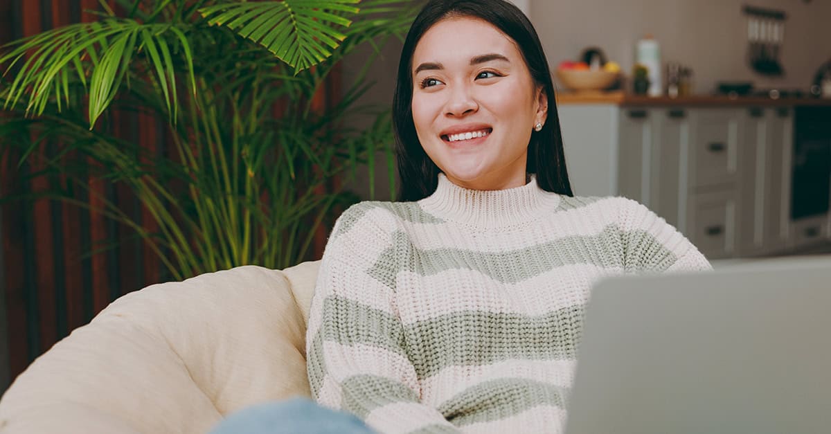 Smiling young Asian woman working on laptop in a casual setting