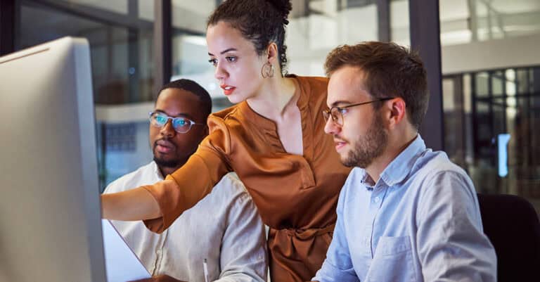Diverse team collaborating, one pointing at data on computer monitor