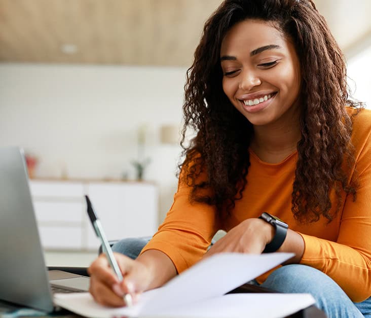 Black woman smiling while writing notes about project